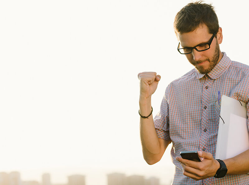 Successful professional casual man gesturing and checking cellphone messages towards city skyline. Entrepreneur enjoys success in job.